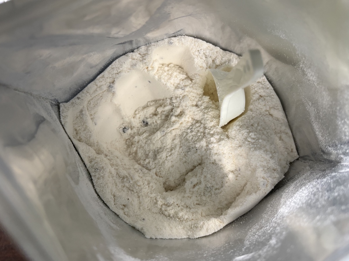 開封した袋の中身。白い粉のなかに黒いチョコチップの粒が点々と混ざり、白いスプーンが半分埋まっている